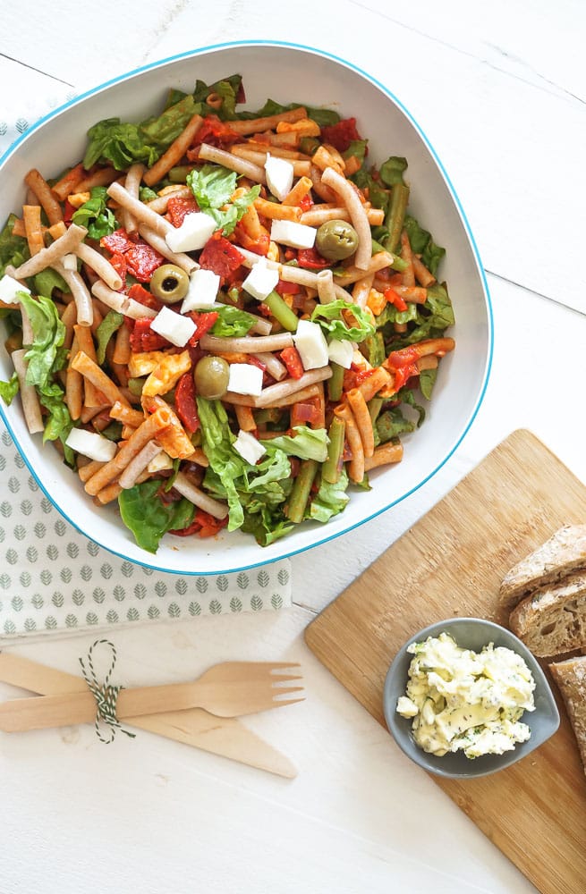 Pastasalade met chorizo, sperziebonen, romaine sla, mozzarella en groene olijven, geserveerd in een grote schaal met een zomerse tomaten-paprika dressing en vers stokbrood – een kleurrijke en smaakvolle maaltijdsalade voor warme dagen.