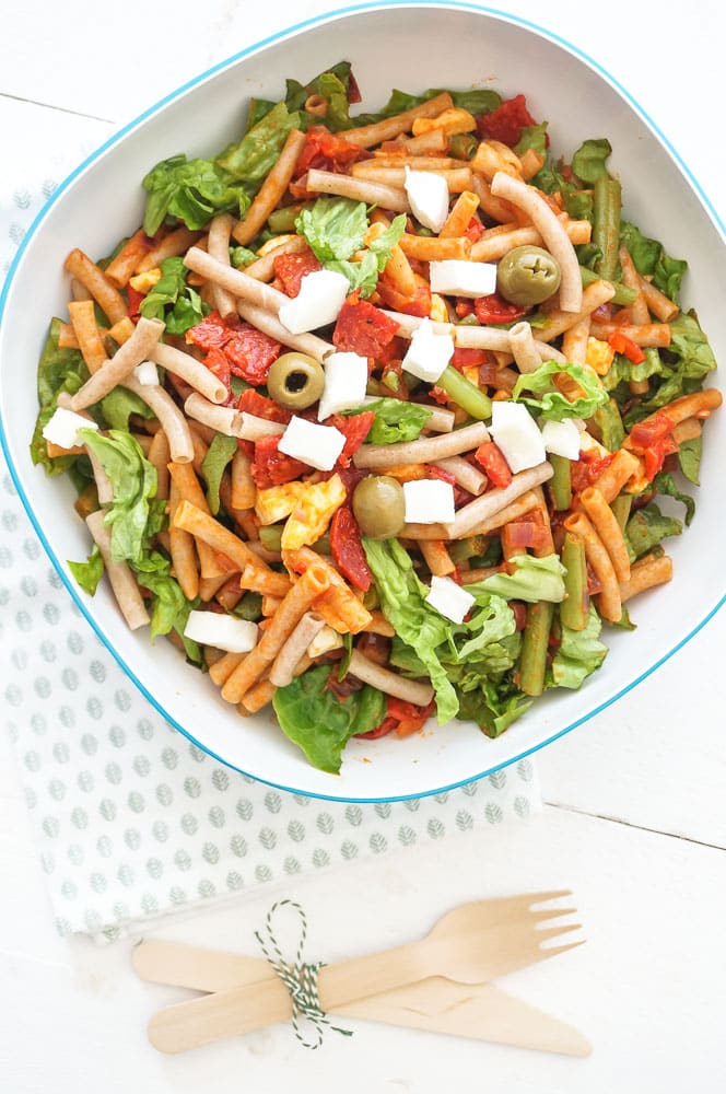 Pastasalade met chorizo, sperziebonen, romaine sla, mozzarella en groene olijven, geserveerd in een grote schaal met een zomerse tomaten-paprika dressing en vers stokbrood – een kleurrijke en smaakvolle maaltijdsalade voor warme dagen.