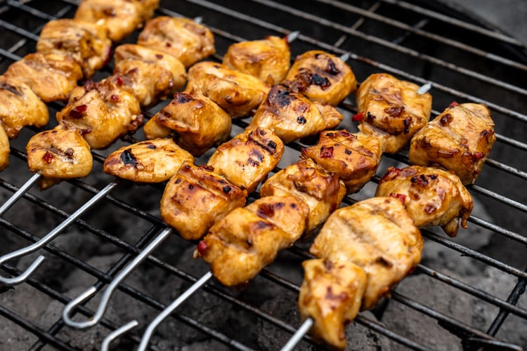 Zelf kipsaté maken. Recept voor geroosterde kipsaté van de BBQ, afgelakt met marinade en geserveerd met satésaus en komkommersalade.