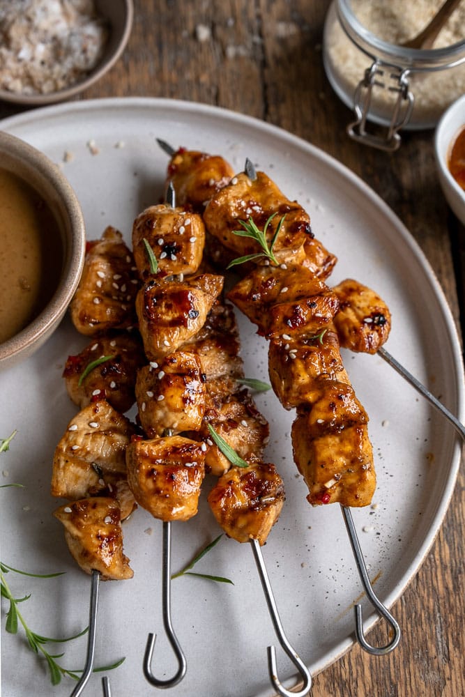 Zelf kipsaté maken. Recept voor geroosterde kipsaté van de BBQ, afgelakt met marinade en geserveerd met satésaus en komkommersalade.