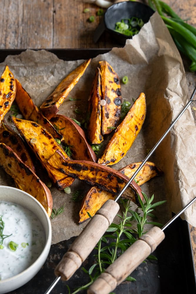Geroosterde zoete aardappel wedges van de BBQ, geserveerd met een frisse yoghurt-dip van dille, citroen en knoflook