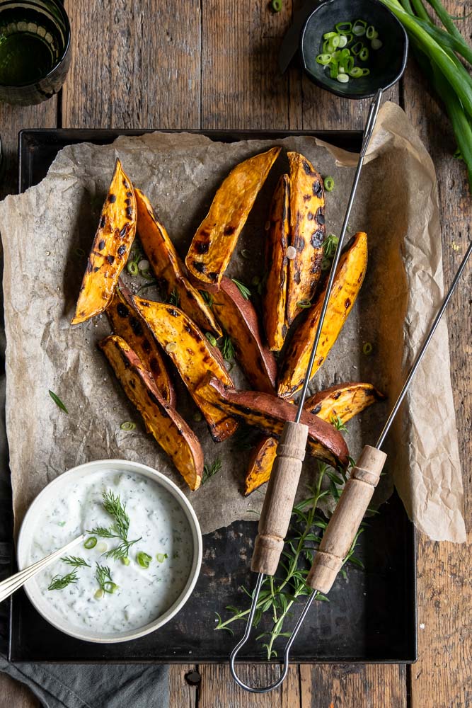 Geroosterde zoete aardappel wedges van de BBQ, geserveerd met een frisse yoghurt-dip van dille, citroen en knoflook