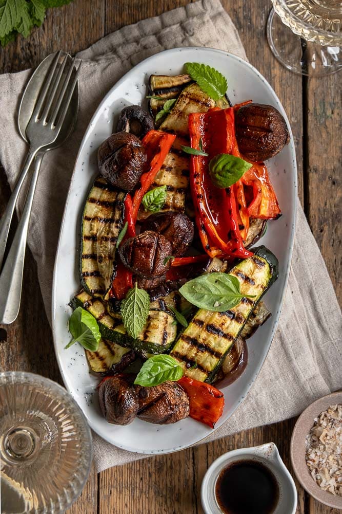 Gegrilde groenten van de barbecue, zoals courgette, paprika, champignons en rode ui, geserveerd met een simpele dressing van balsamico, mosterd, olijfolie en knoflook – zomers, smaakvol en kleurrijk bijgerecht.