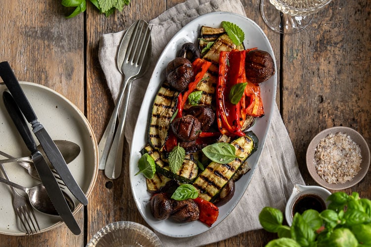 Gegrilde groenten van de barbecue, zoals courgette, paprika, champignons en rode ui, geserveerd met een simpele dressing van balsamico, mosterd, olijfolie en knoflook – zomers, smaakvol en kleurrijk bijgerecht.