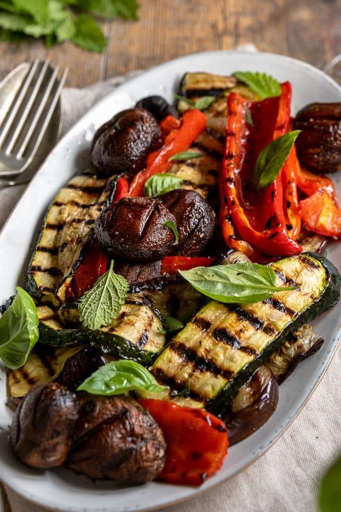 Gegrilde groenten van de barbecue, zoals courgette, paprika, champignons en rode ui, geserveerd met een simpele dressing van balsamico, mosterd, olijfolie en knoflook – zomers, smaakvol en kleurrijk bijgerecht.
