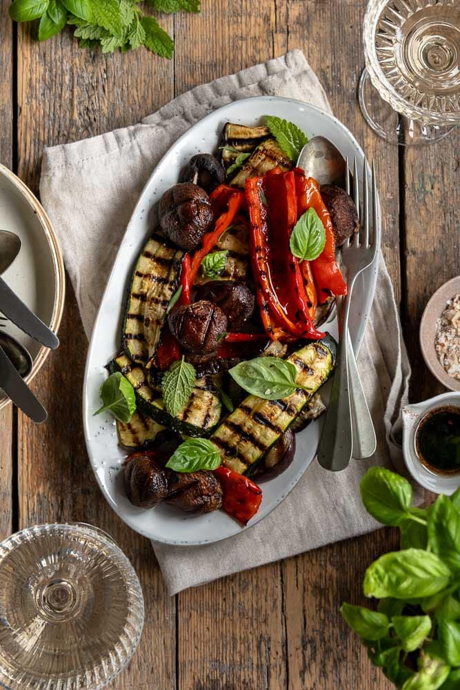 Gegrilde groenten van de barbecue, zoals courgette, paprika, champignons en rode ui, geserveerd met een simpele dressing van balsamico, mosterd, olijfolie en knoflook – zomers, smaakvol en kleurrijk bijgerecht.