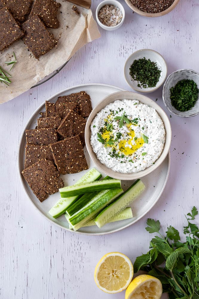 Romige cottage cheese dip met olijfolie, citroen en verse kruiden in een schaaltje, geserveerd met rauwkost en crackers — eiwitrijke, gezonde dip. Whipped cottage cheese.