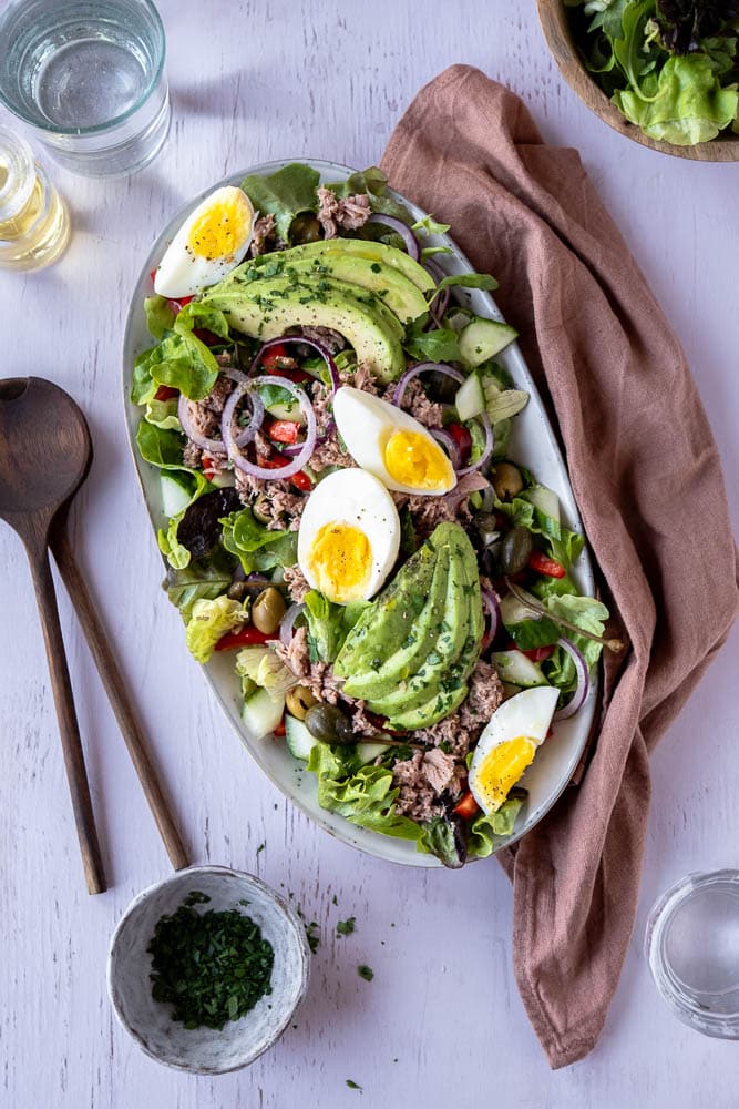 Salade met tonijn, avocado en ei op een bord met verse groenten, paprika, rode ui en groene olijven – makkelijke lunchsalade met tonijn uit blik.