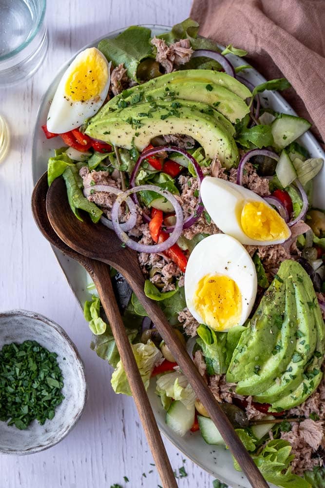 Salade met tonijn, avocado en ei op een bord met verse groenten, paprika, rode ui en groene olijven – makkelijke lunchsalade met tonijn uit blik.