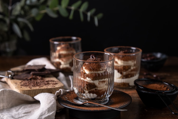 Tiramisu in een glaasje met mascarpone, slagroom, lange vingers en cacao; feestelijk Italiaans dessert geserveerd in laagjes.