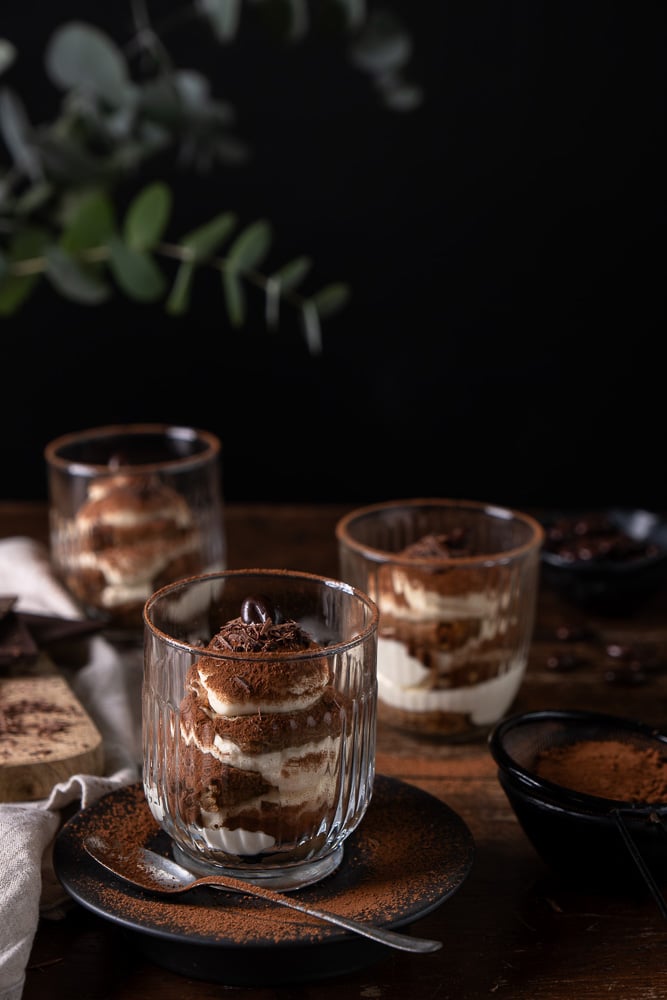 Tiramisu in een glaasje met mascarpone, slagroom, lange vingers en cacao; feestelijk Italiaans dessert geserveerd in laagjes.