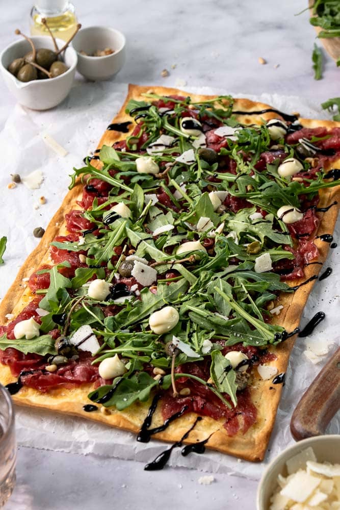 Flammkuchen met carpaccio, rucola en Parmezaanse kaas op een dunne, krokante bodem; feestelijk borrelhapje voor kerst of Oud & Nieuw.
