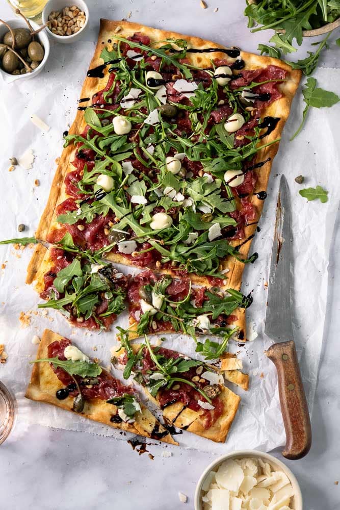 Flammkuchen met carpaccio, rucola en Parmezaanse kaas op een dunne, krokante bodem; feestelijk borrelhapje voor kerst of Oud & Nieuw.