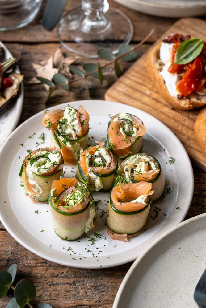 Komkommerrolletjes met zalm en roomkaas, opgerold tot frisse hapjes en gegarneerd met dille.