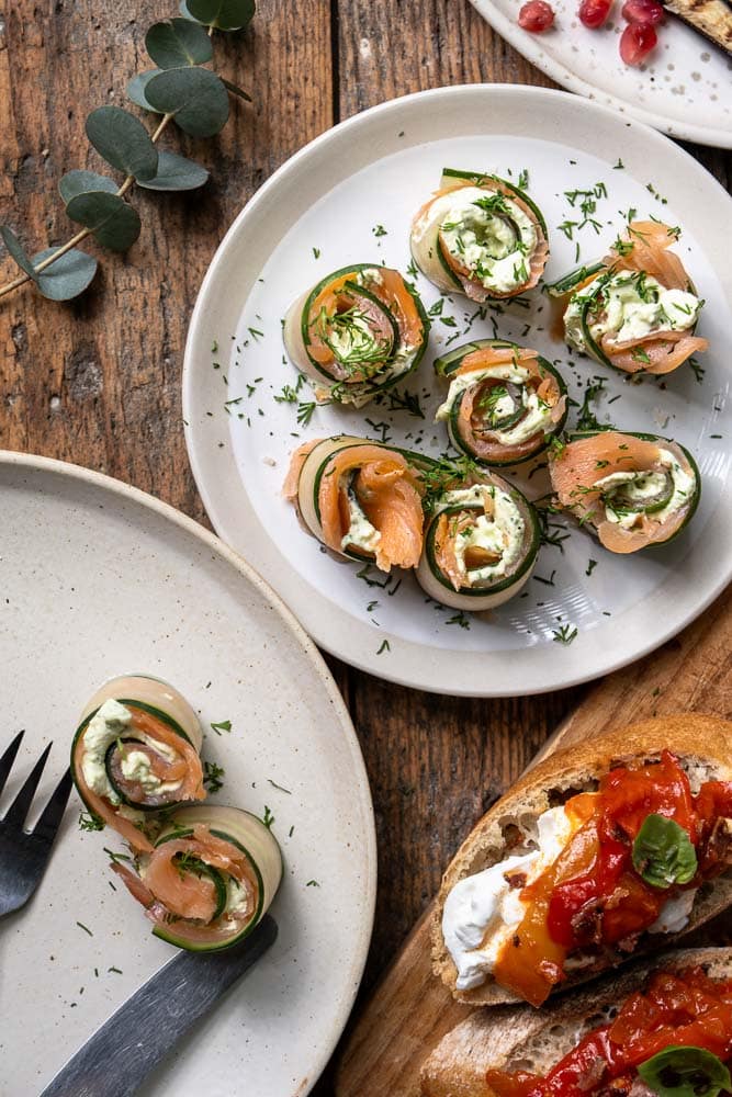 Komkommerrolletjes met zalm en roomkaas, opgerold tot frisse hapjes en gegarneerd met dille.
