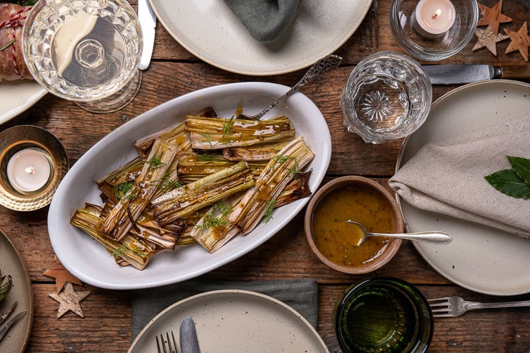 Prei uit de oven; gehalveerde prei geroosterd met olijfolie, peper en zout, zacht en licht gekaramelliseerd, geserveerd met honing-mosterd dressing als smaakvol groente bijgerecht.