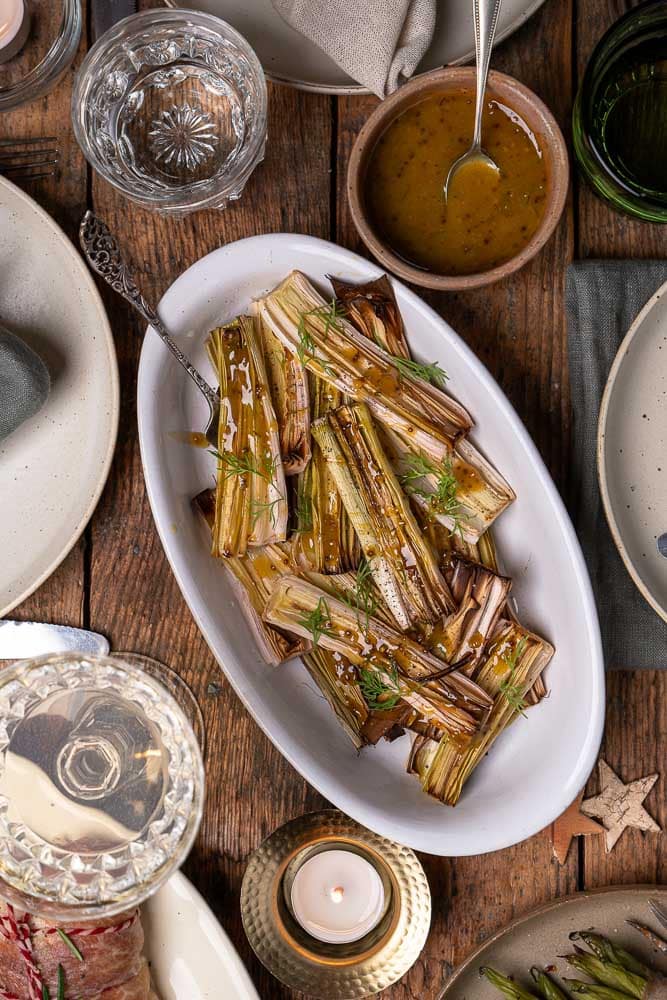 Prei uit de oven; gehalveerde prei geroosterd met olijfolie, peper en zout, zacht en licht gekaramelliseerd, geserveerd met honing-mosterd dressing als smaakvol groente bijgerecht.