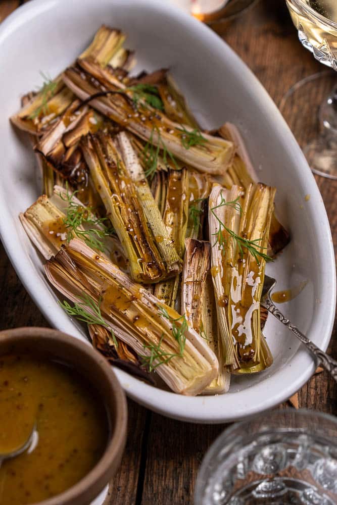 Prei uit de oven; gehalveerde prei geroosterd met olijfolie, peper en zout, zacht en licht gekaramelliseerd, geserveerd met honing-mosterd dressing als smaakvol groente bijgerecht.
