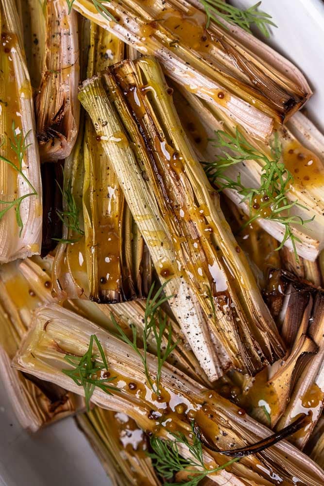 Prei uit de oven; gehalveerde prei geroosterd met olijfolie, peper en zout, zacht en licht gekaramelliseerd, geserveerd met honing-mosterd dressing als smaakvol groente bijgerecht.