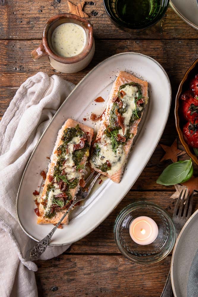 Zalmfilet ingesmeerd met groene pesto en bedekt met krokante hamkruimels, klaar om in de oven te garen.