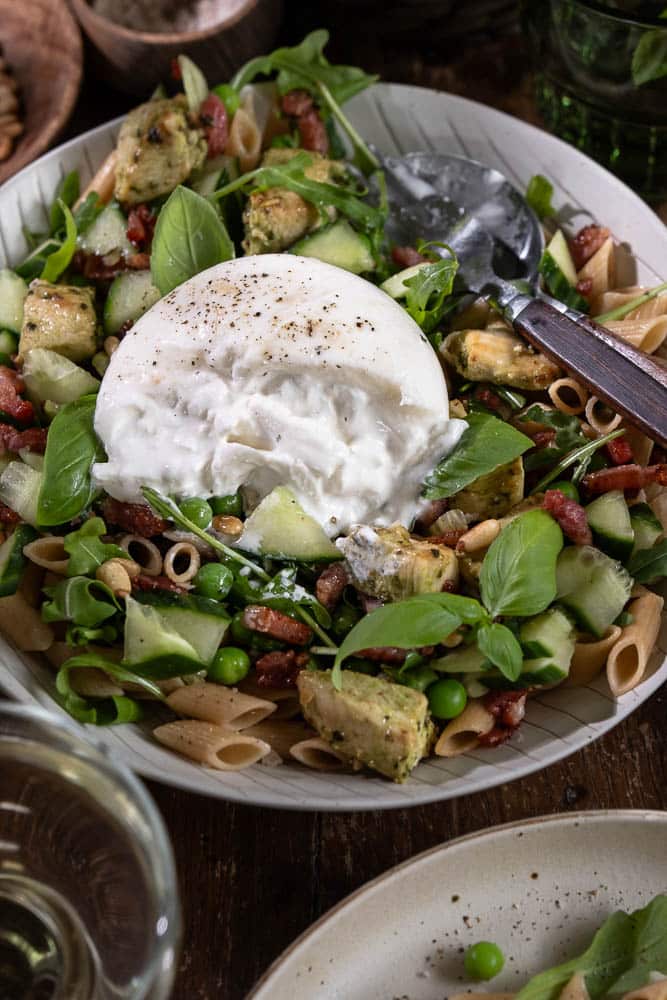 Pastasalade met kip, volkoren pasta, burrata, pesto, spekjes, rucola en doperwten. Makkelijke Italiaanse maaltijdsalade voor lunch of avondeten.